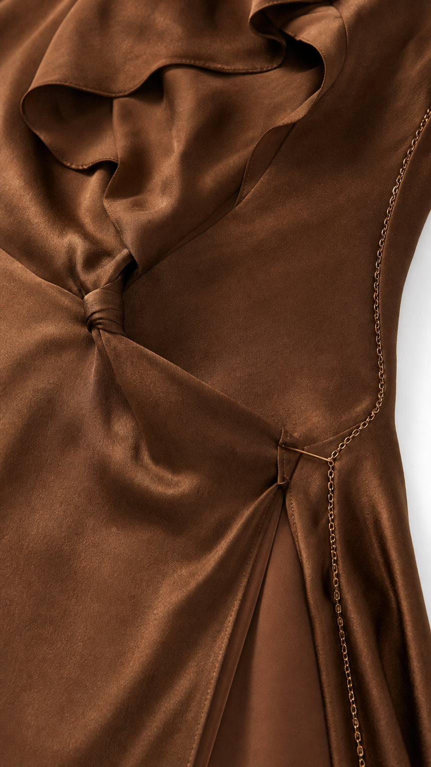 Close-up detail of brown satin fabric showing ruffled neckline, knot waist, and delicate chain accent