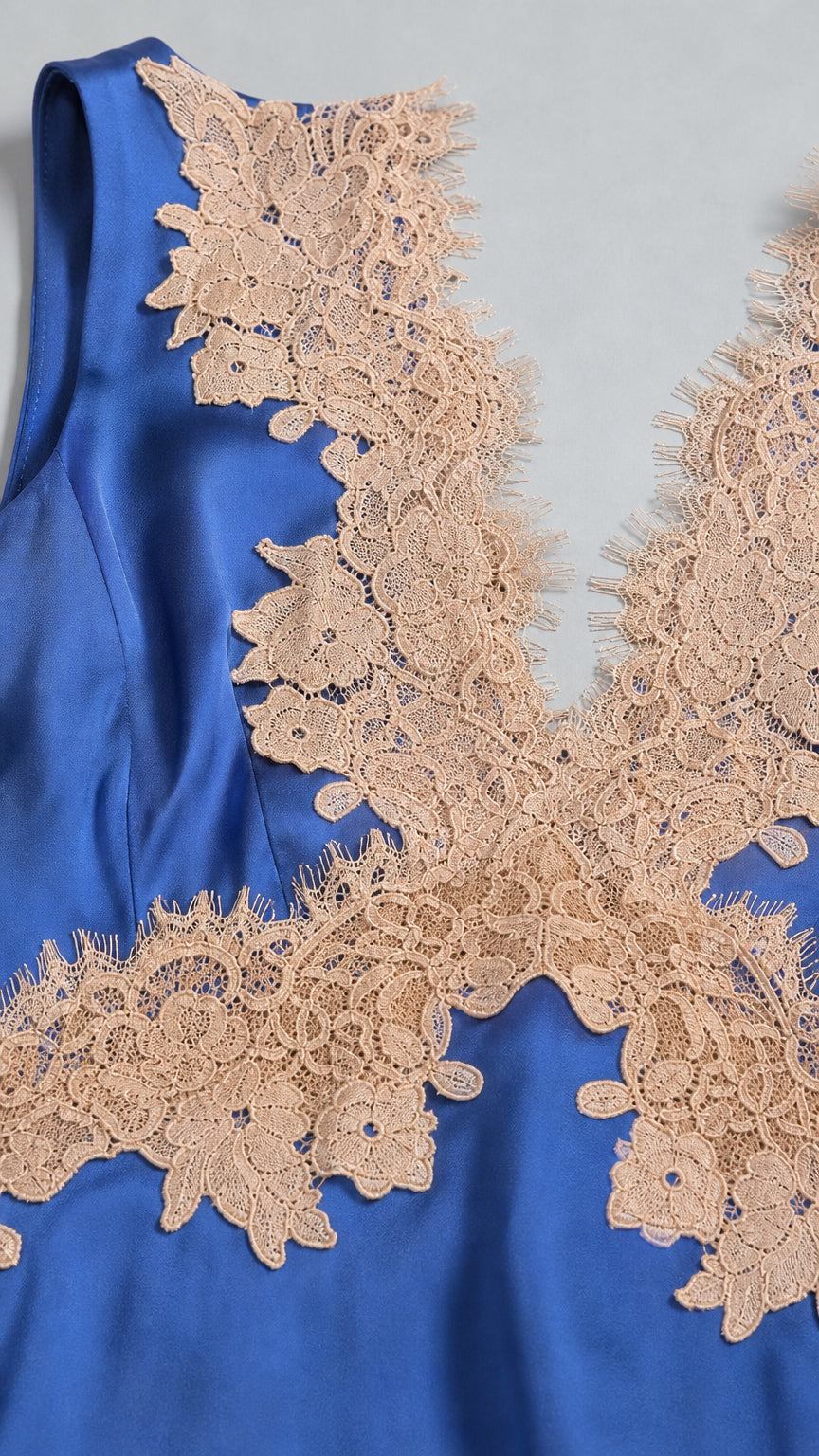 Close-up detail of champagne floral lace applique on royal blue satin fabric