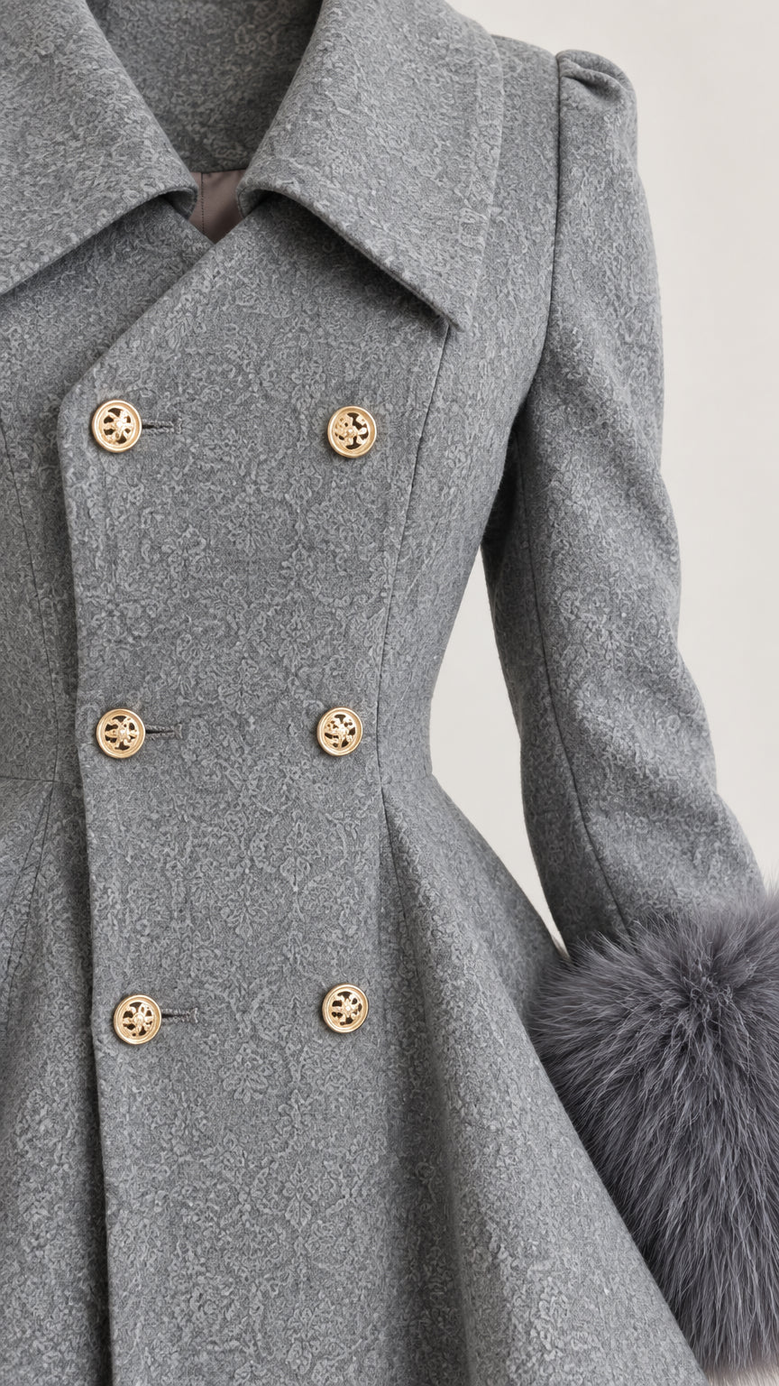 Close up detail of textured grey fabric, gold-tone crest buttons, lapel collar, and faux fur cuff