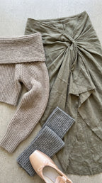 Flat lay detail of sage green knit sweater, draped wrap skirt, grey leg warmers, and ballet shoes
