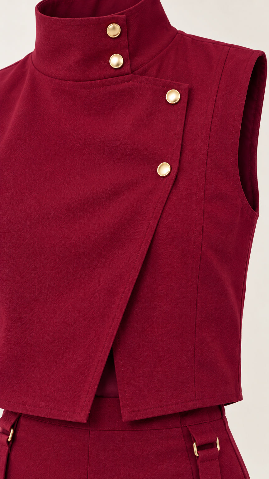 Close-up detail of burgundy high-neck asymmetric top featuring gold-tone buttons and strap detail