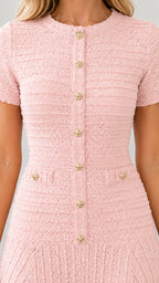 Close-up detail of textured blush pink tweed fabric and embossed gold buttons