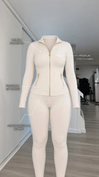 Product diagram highlighting gold zipper, functional zip pockets, and structural seaming on cream tracksuit set