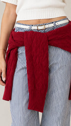 Close-up detail of waistline showing white belt, vertical striped trousers, and tied red knit sweater