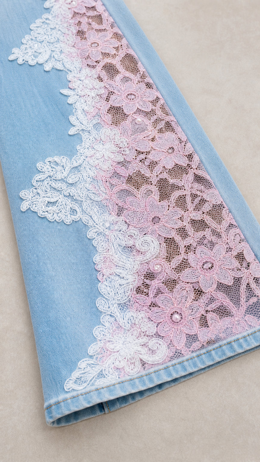 Close-up detail of light blue denim hem with delicate floral lace applique