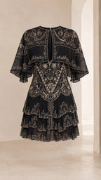 Flat front view of black embroidered capelet tiered mini dress showing filigree patterns