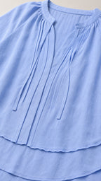 Close-up detail of pleated notch neckline and double-layered tiered hem on Light Blue blouse