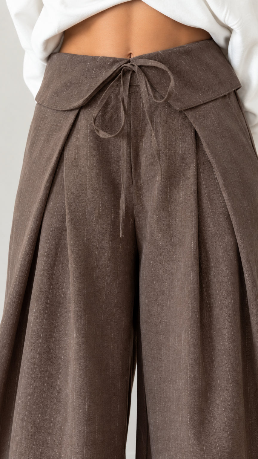 Close-up detail of brown fold-over crossover waistband with self-tie string and pleats