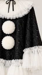 Close-up detail of textured black sequin fabric, tiered white tulle collar with black bow, and fluffy pom-pom accents
