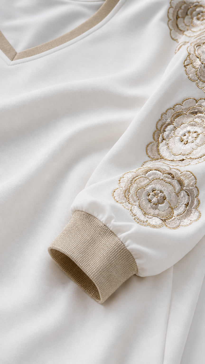 Close-up detail of metallic knit cuff, ivory fabric, and gold floral embroidery
