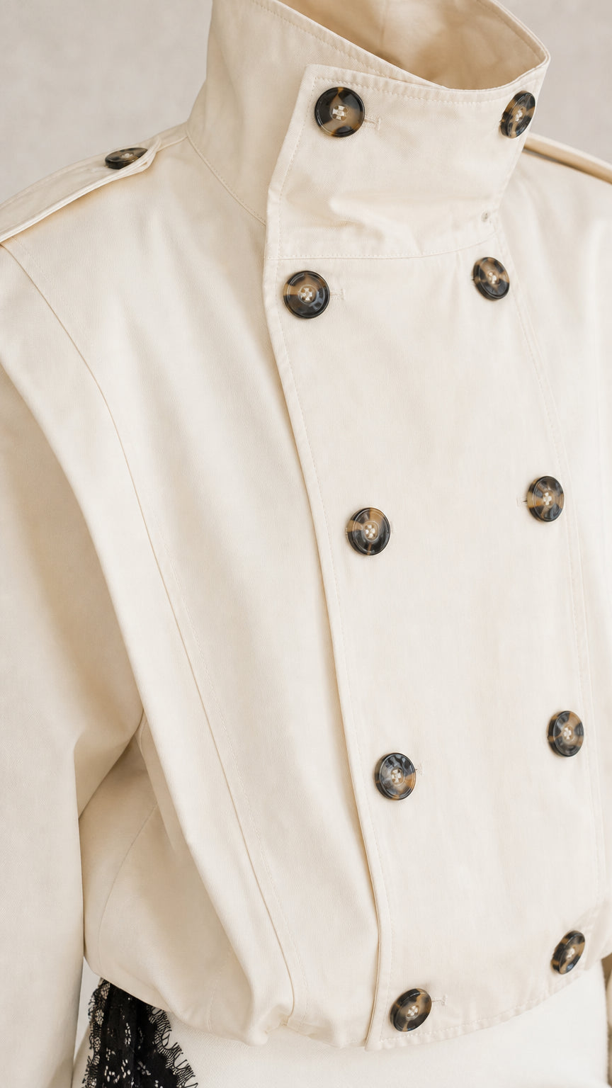 Close-up detail of cream high stand collar and tortoiseshell double-breasted buttons