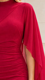 Close-up detail of the red dress showing the ruched bodice texture and sheer cape fabric