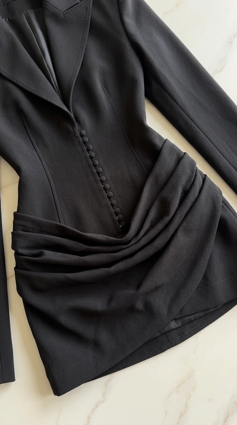Close-up detail of black blazer dress showing lapel collar, covered buttons, and draped ruching