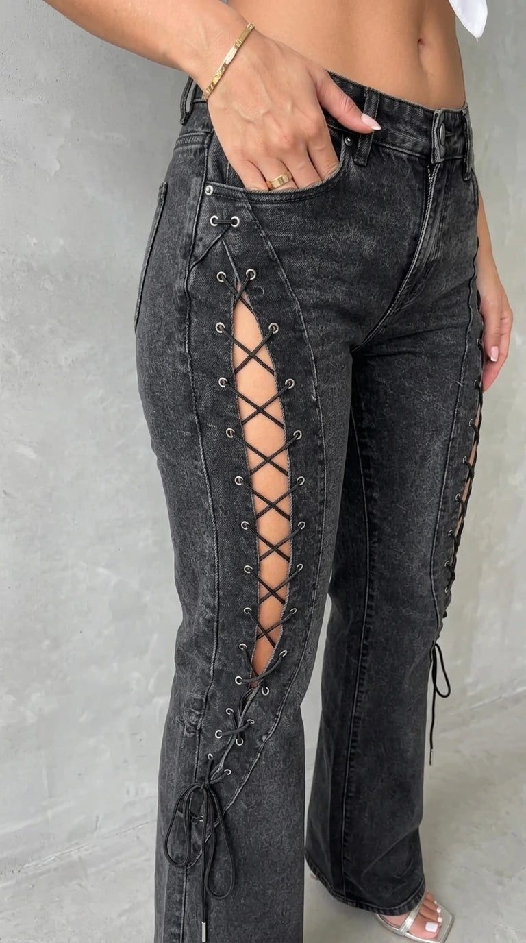 Close-up detail shot of metal grommets and lace-up cutout detail on the side of washed black denim jeans