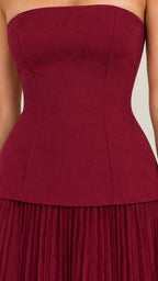 Close-up detail of structured burgundy corset bodice and drop waist pleated skirt seam
