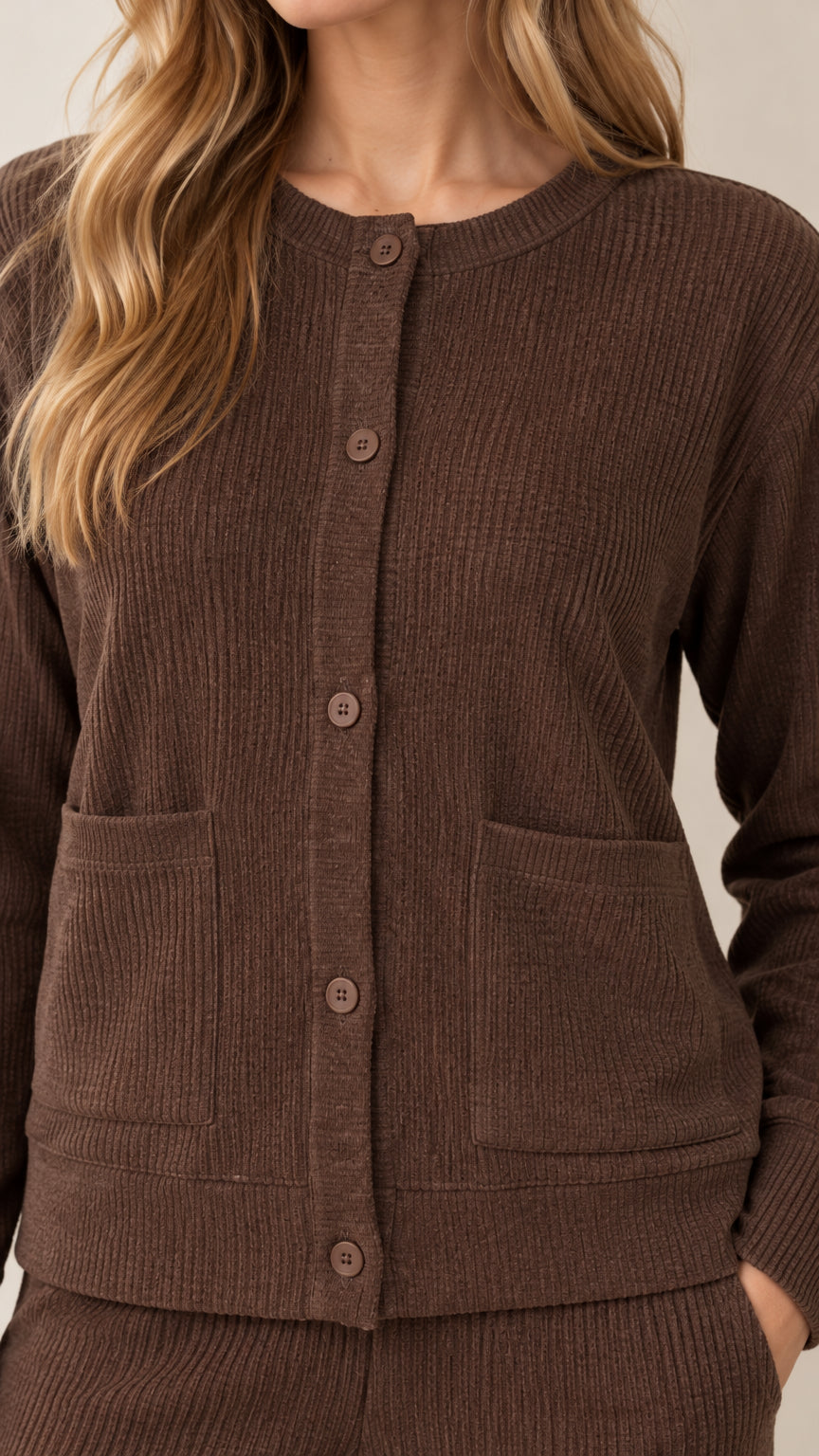Close-up detail of brown ribbed knit cardigan showing buttons, neckline, and patch pocket