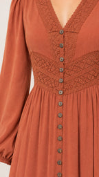 Close-up detail of V-neckline, crochet lace waist panel, and buttons on rust orange dress