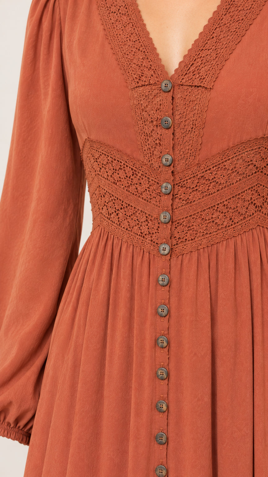 Close-up detail of V-neckline, crochet lace waist panel, and buttons on rust orange dress