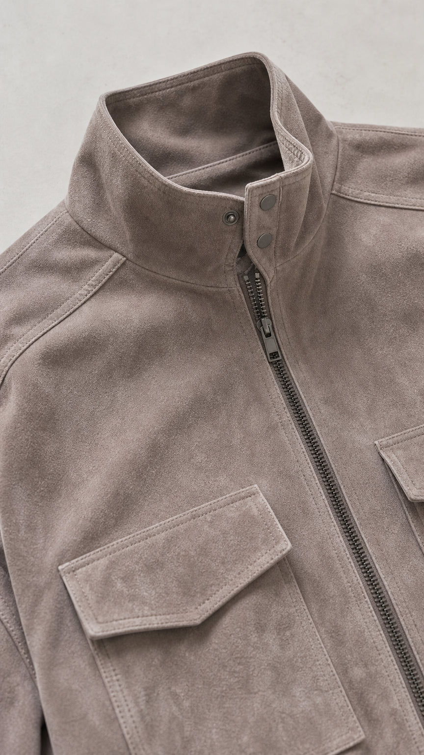 Close-up detail of stand collar, zipper closure, and chest flap pocket on taupe jacket