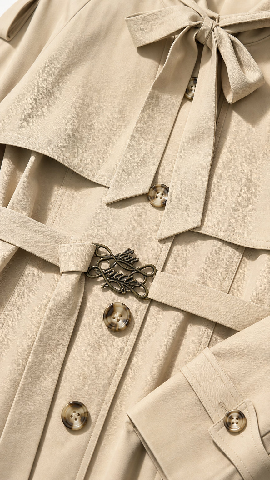 Close-up detail of beige trench coat neckline tie, buttons, and decorative buckle belt