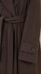 Close-up detail of dark brown coat fabric, buttons, and sleeve cuff tab