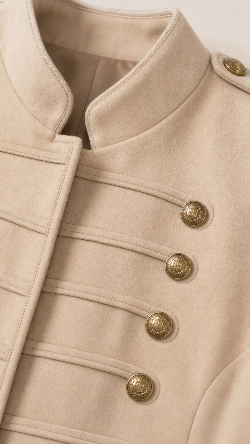 Close-up detail of beige fabric, stand collar, epaulet, and ornate brass buttons