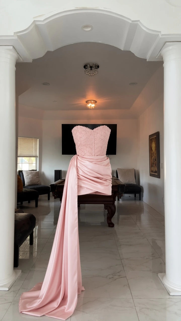 Mannequin display of blush pink strapless mini dress with long side sash train