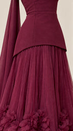 Close-up detail of burgundy gown showing the smooth peplum bodice waistline and textured 3D flower appliques on the pleated tulle skirt