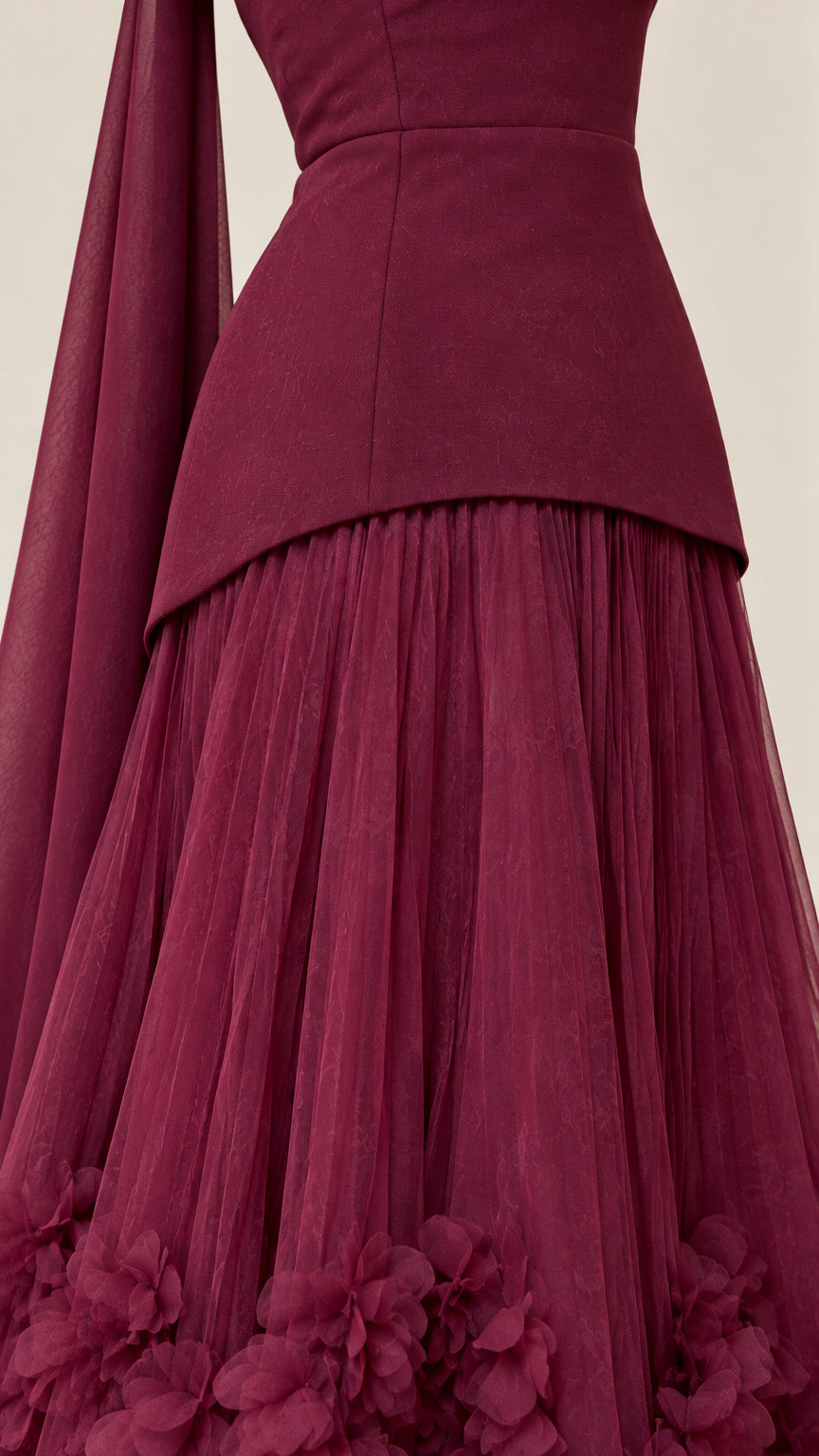 Close-up detail of burgundy gown showing the smooth peplum bodice waistline and textured 3D flower appliques on the pleated tulle skirt