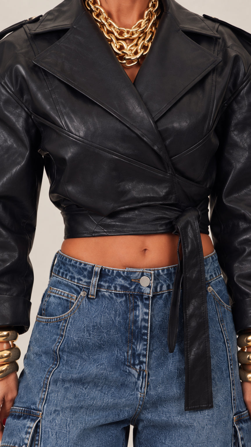 Close-up of black cropped faux leather wrap jacket showing notched lapel and tie waist detail