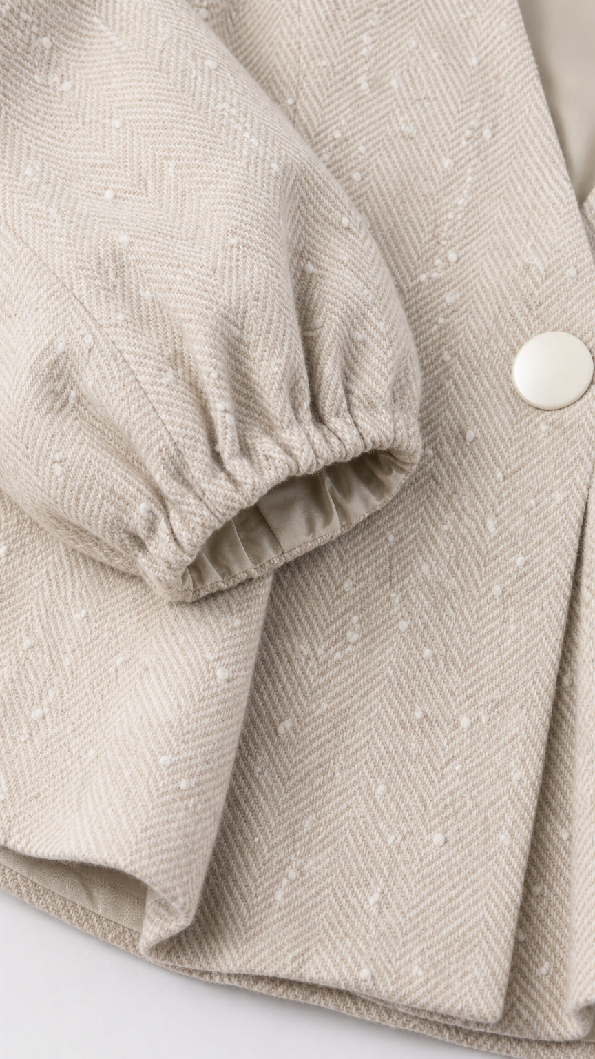 Close-up detail of beige tweed woven fabric, single button, and gathered sleeve cuff
