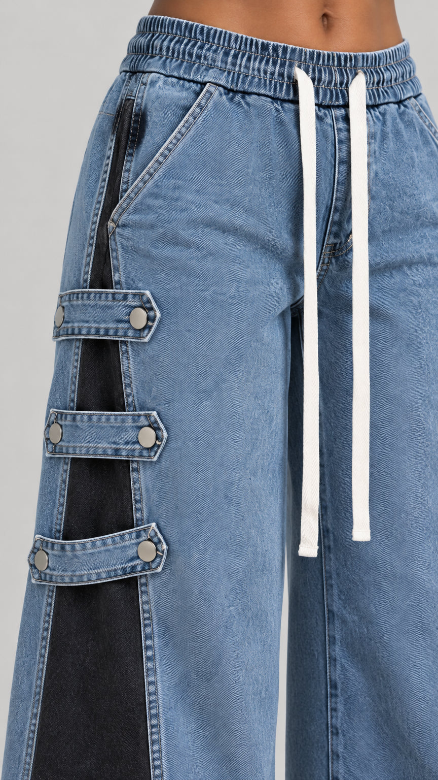 Close-up detail of gathered elastic waistband, white drawstring, and side snap buckle tabs