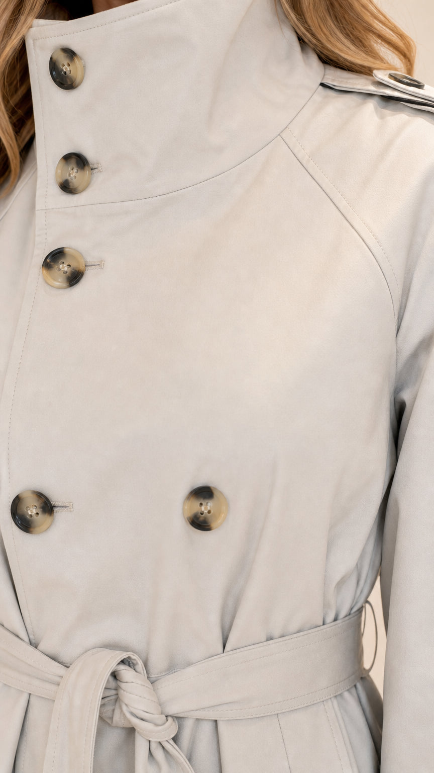 Close up view of high stand collar and tortoiseshell buttons on light grey trench jacket