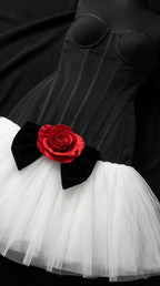 Close-up of black boned corset bodice with black bow and red rose appliqué over white tulle