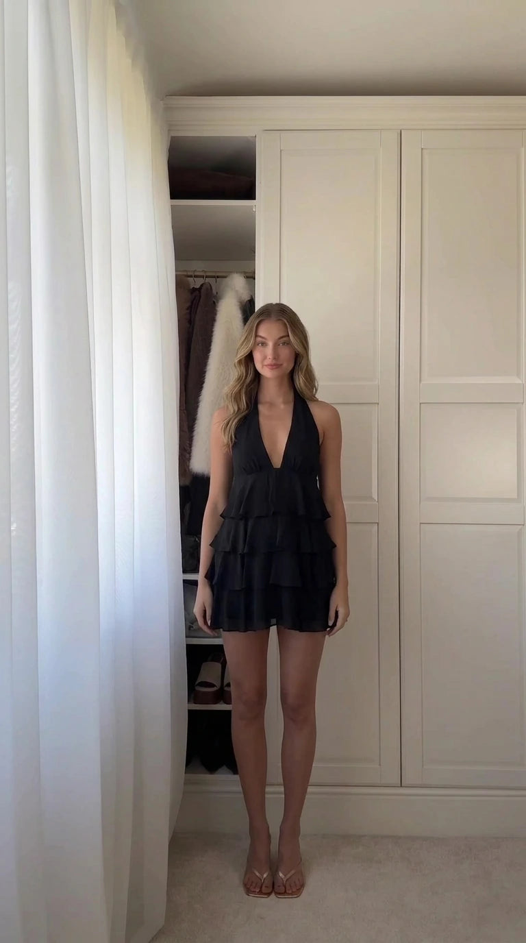 Front view of woman wearing black halter neck tiered ruffle mini dress