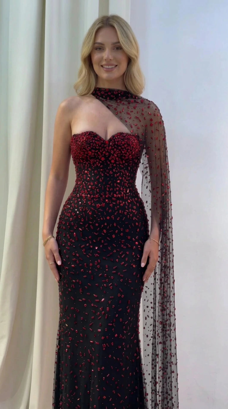 Model wearing black and red beaded asymmetric cape evening gown