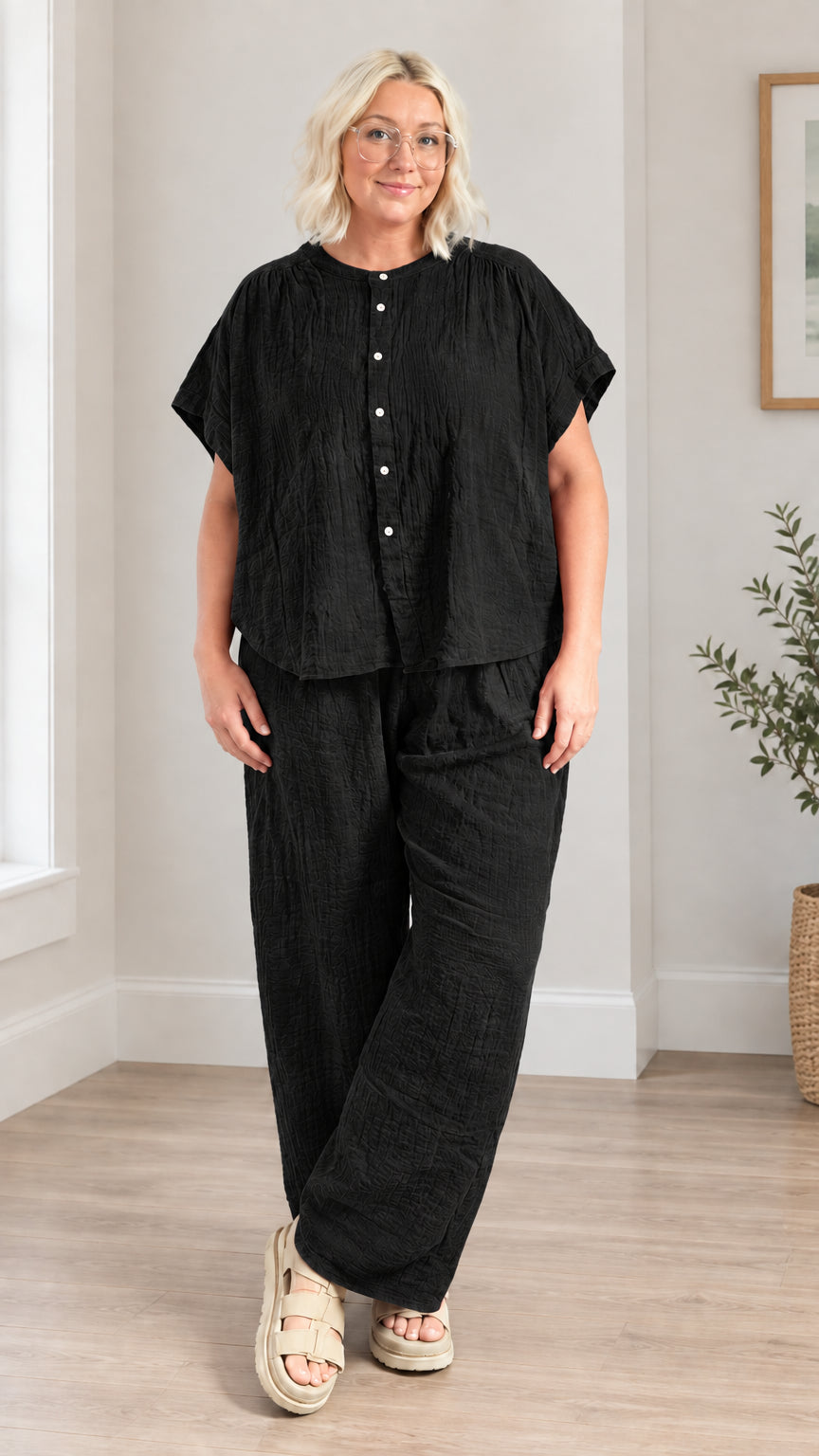 Model wearing black short-sleeve button top and matching wide leg pants two-piece set