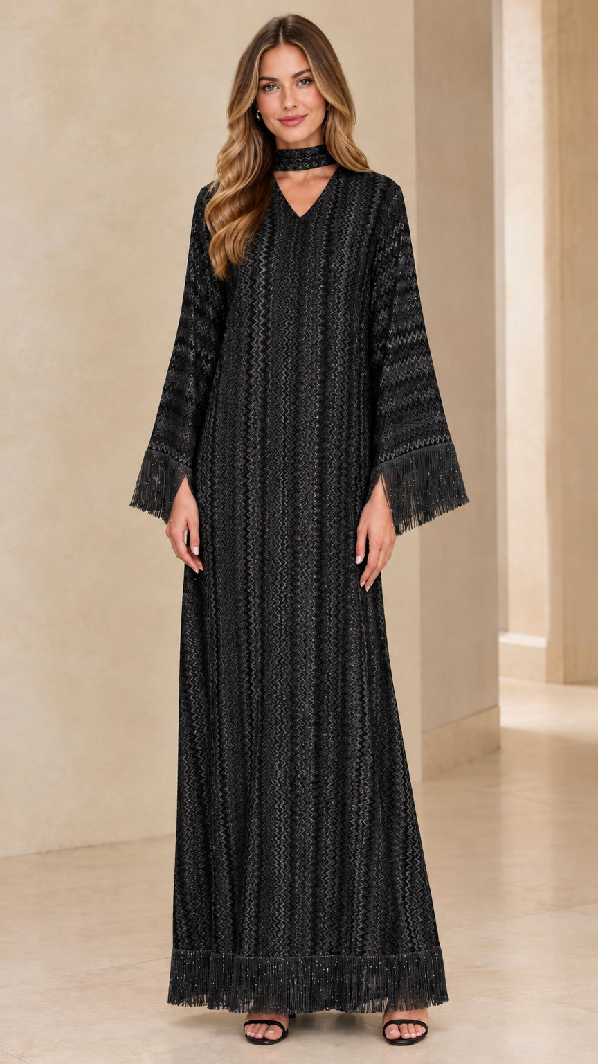 Front view of woman wearing black textured chevron long sleeve maxi dress with fringe detailing