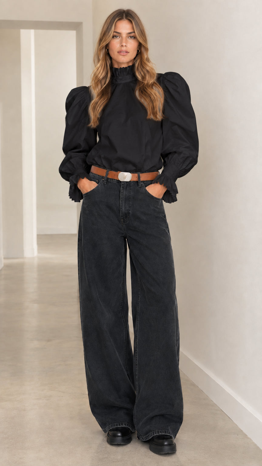 Woman wearing black ruffle high-neck puff-sleeve blouse tucked into dark wide-leg trousers