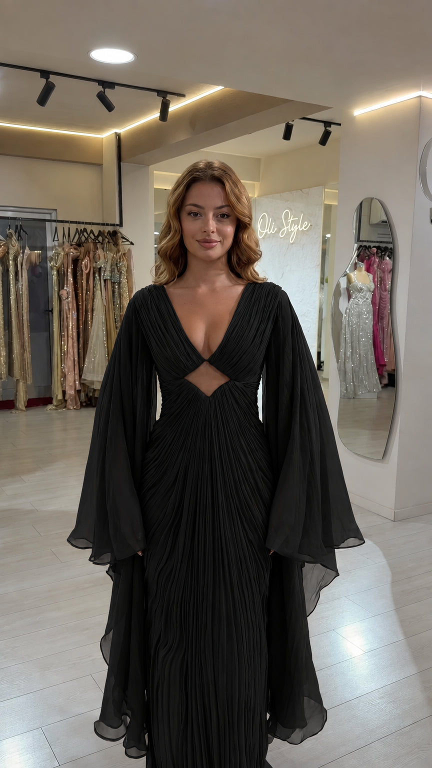 Full front view of black pleated cutout evening gown with dramatic cape sleeves