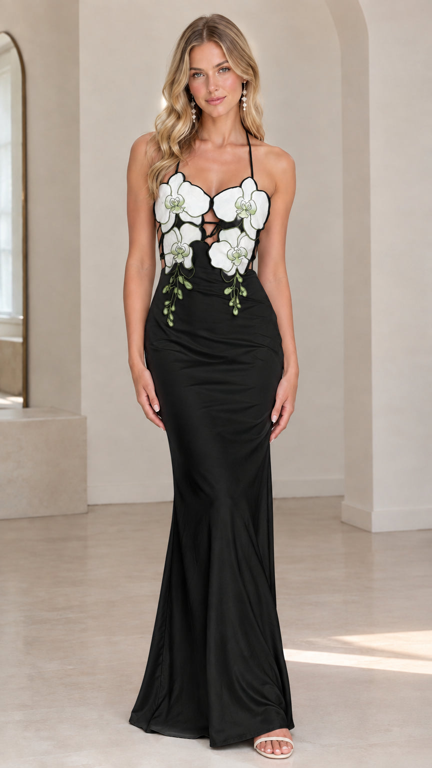 Front view of model wearing black satin halter maxi dress with white floral appliqués