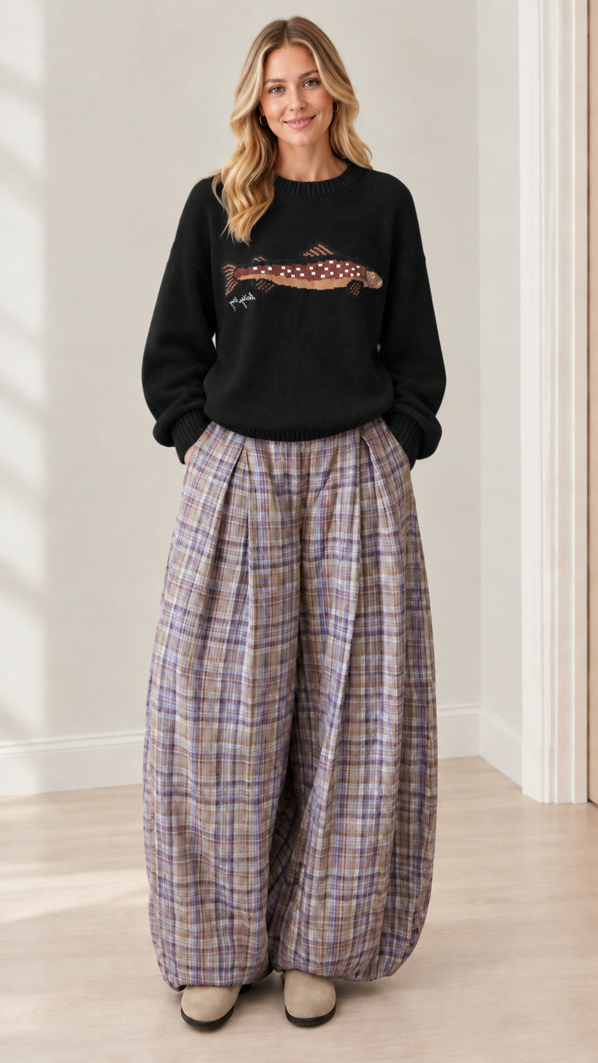Model wearing black graphic knit sweater paired with pleated plaid balloon pants