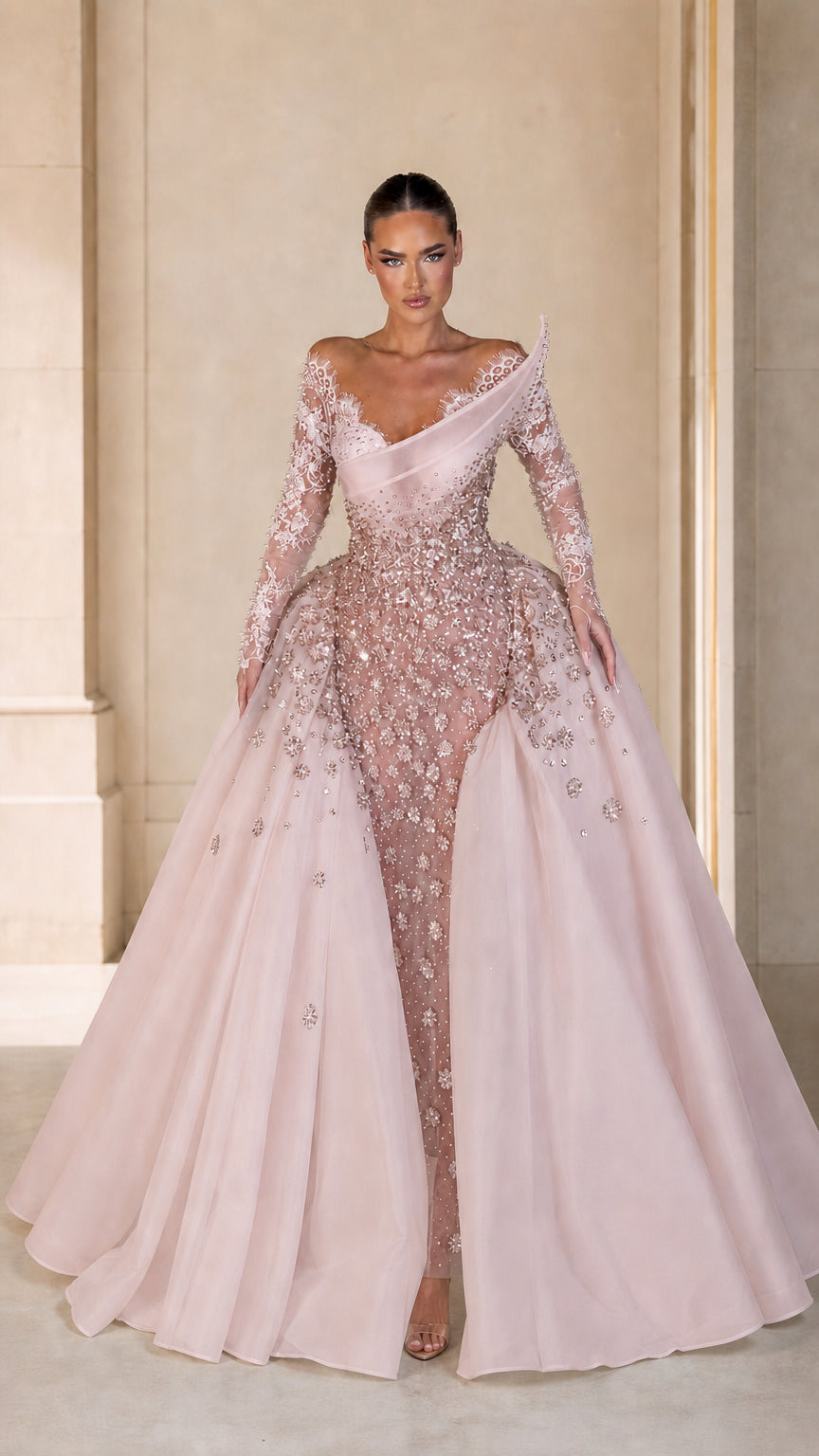 Front view of model in blush pink beaded evening gown with long sleeves and pleated overskirt