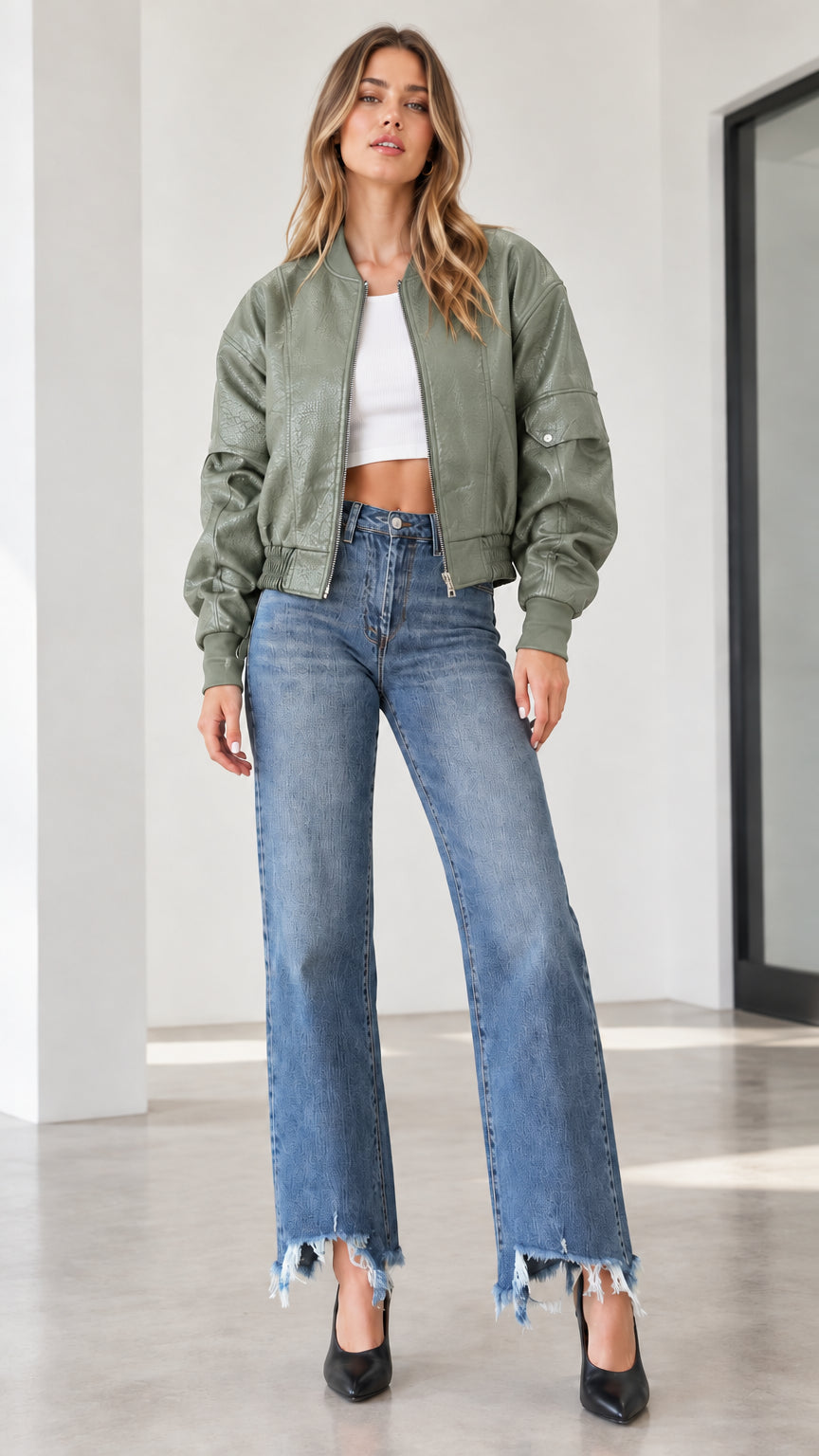 Model wearing a sage green textured faux leather bomber jacket with wide-leg denim
