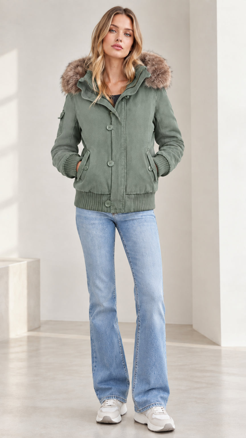 Front view of model wearing sage green fleece-lined hooded bomber jacket with flare jeans