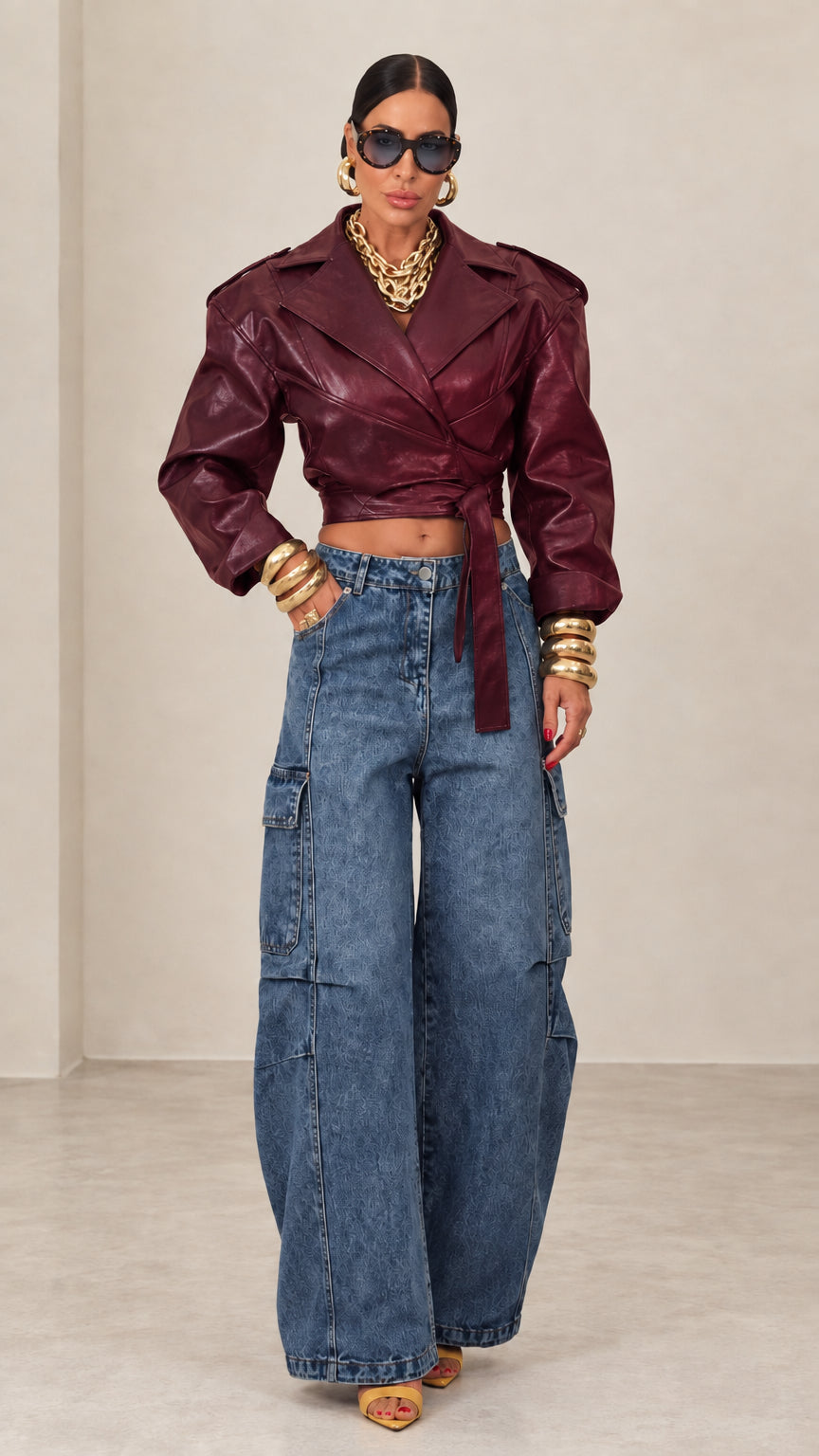 Model wearing burgundy cropped faux leather wrap jacket paired with blue denim jeans