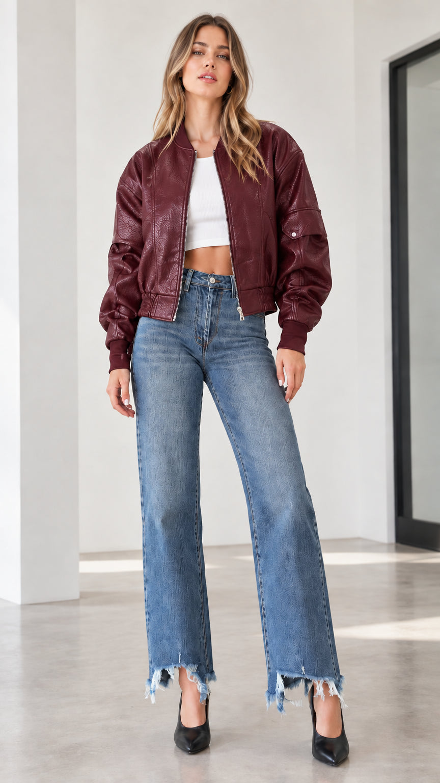 Model wearing a burgundy wine red textured faux leather bomber jacket with wide-leg denim