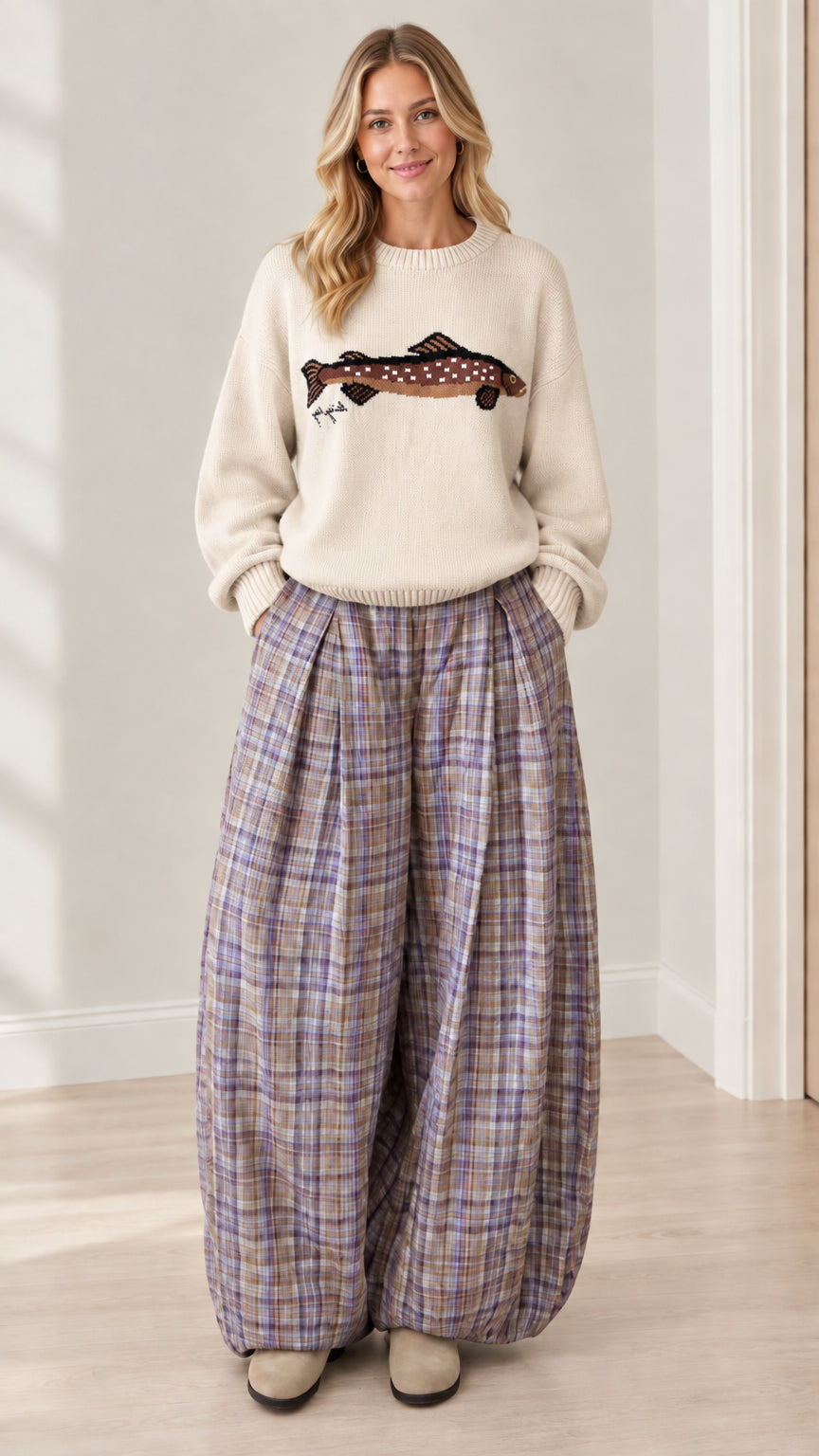 Model wearing cream knit sweater with fish graphic and plaid pleated pants