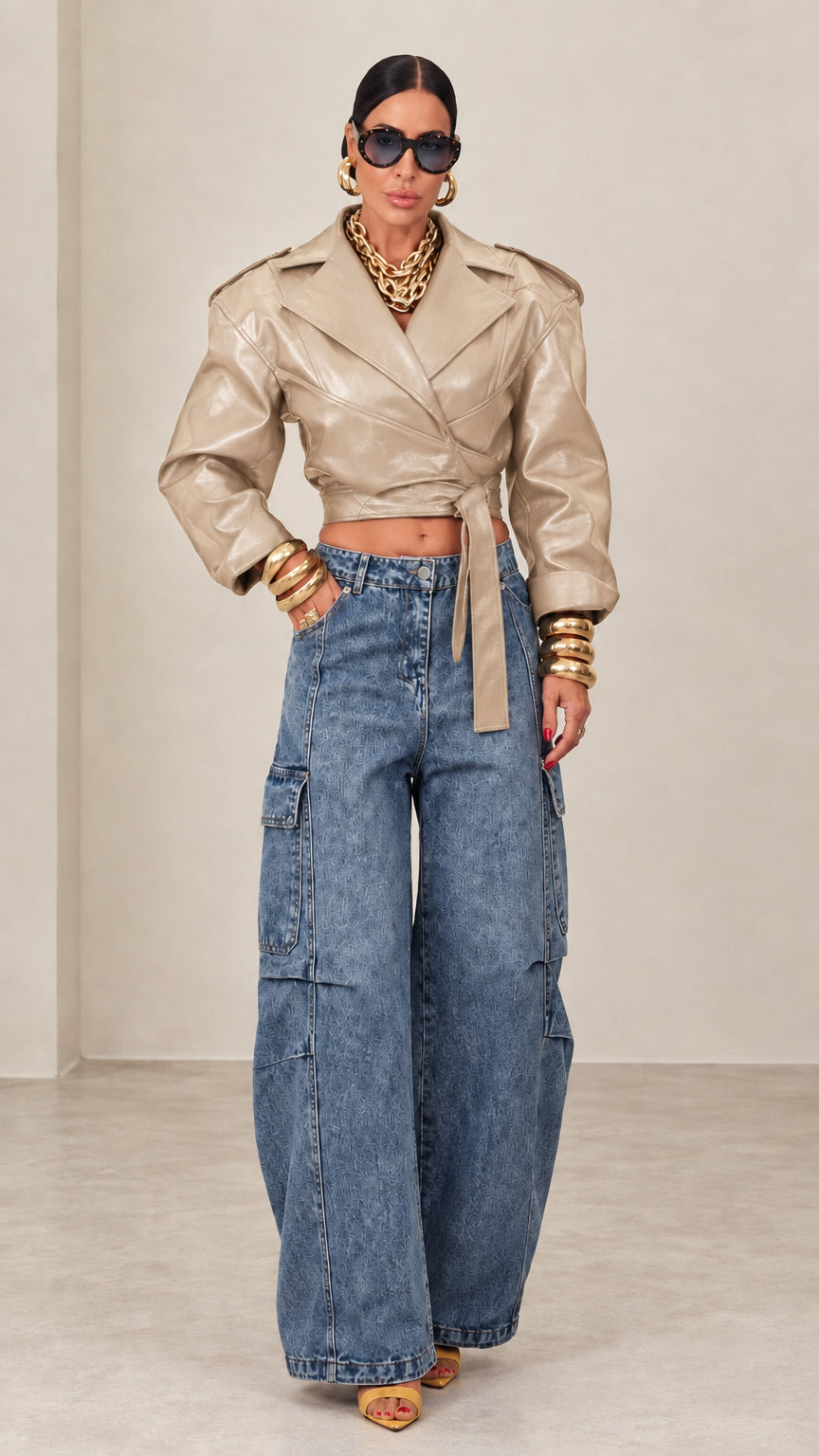 Model wearing beige cropped faux leather wrap jacket with blue wide-leg denim jeans